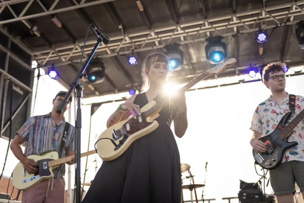 A band performs on stage with multiple musicians playing guitars and singing under professional lighting.