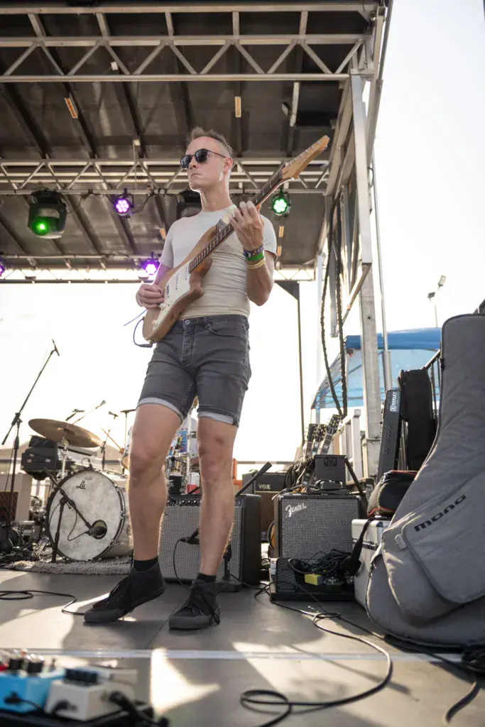 A guitarist in sunglasses performs on stage under professional lighting at an outdoor music festival.
