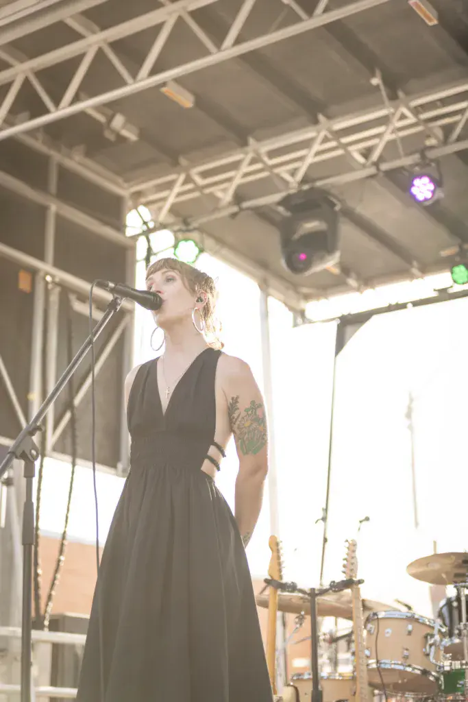 A performer singing at a microphone on an outdoor stage with colorful stage lighting overhead.