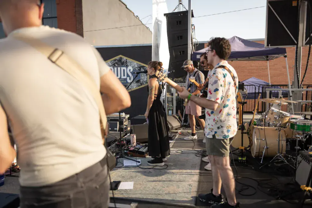 Band members perform on an outdoor stage at Dancing Rabbit Music Festival while audience members watch from the side.
