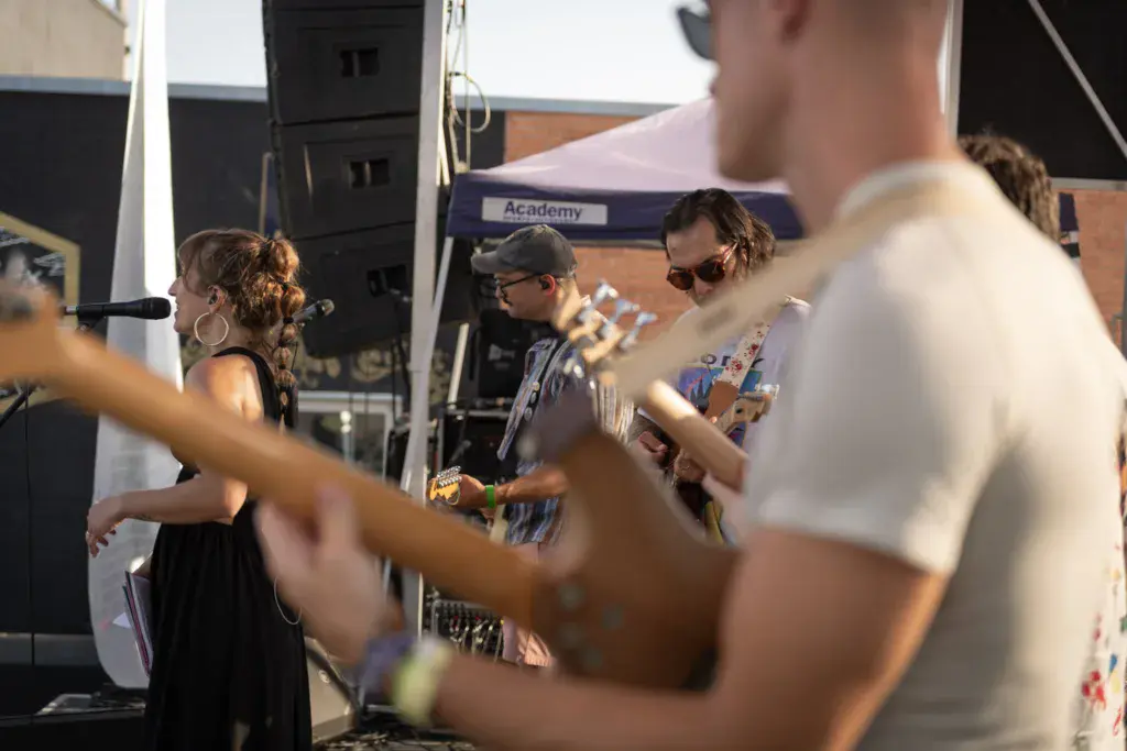 A performer sings on stage while audience members dance and enjoy the music at an outdoor festival.