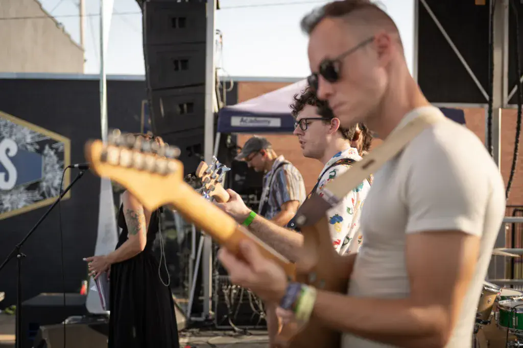 Musicians perform on stage at an outdoor music festival with band members playing guitars and other instruments.