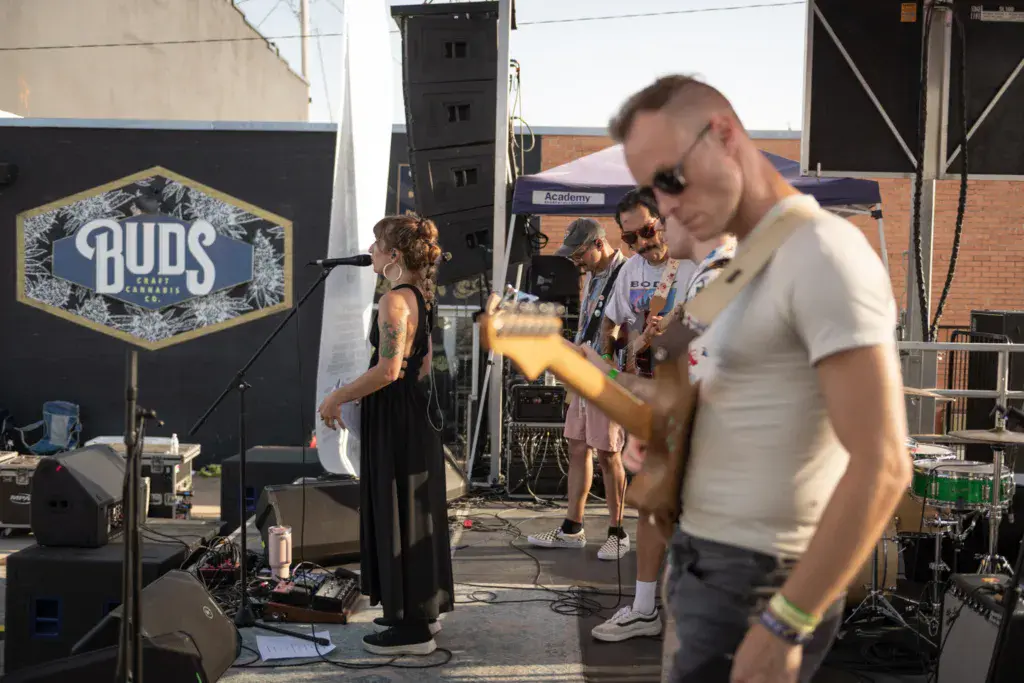 Band members perform on stage with a Buds beer sponsor banner visible in the background.