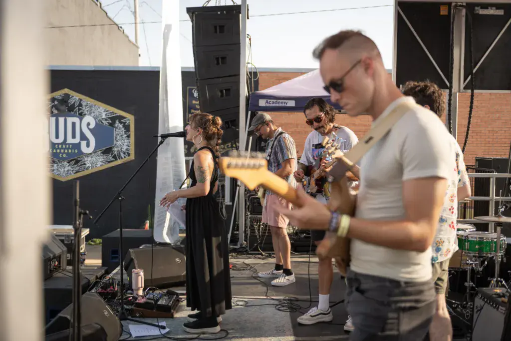 A band performs on stage at an outdoor festival while audience members watch and dance in front of them.