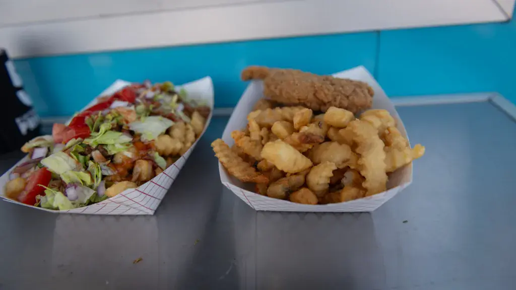 Two paper containers of festival food on a gray table with a blue vendor structure behind them.