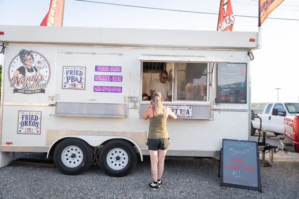 A person in a yellow tank top stands at the service window of Nanny's Kitchen food truck at the festival.