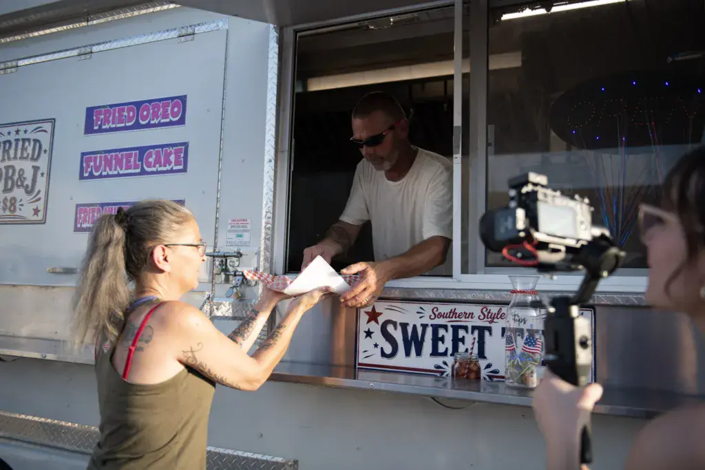 A customer receives food from a vendor at a food truck window labeled Southern Style Sweet.