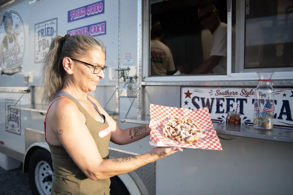 A vendor at a food truck holds a plate of Southern-style food at an outdoor music festival.