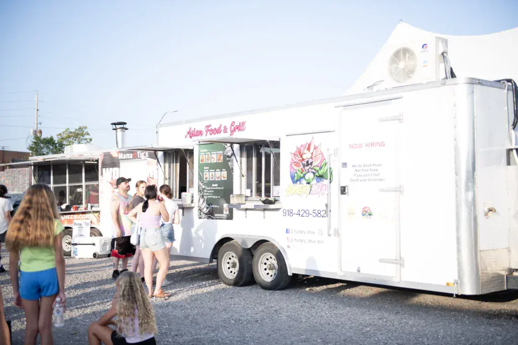 Festival attendees queue at a white food truck called Asian Food & Grill on a sunny day.