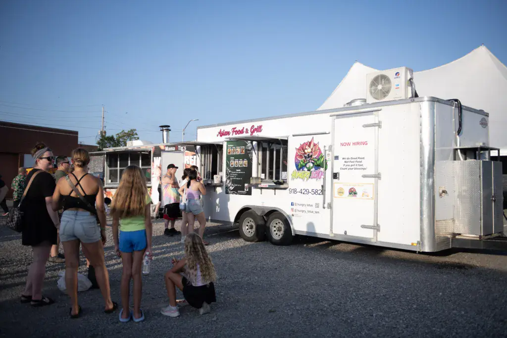 Festival attendees queue outside an Asian food truck with white tent visible in the background.