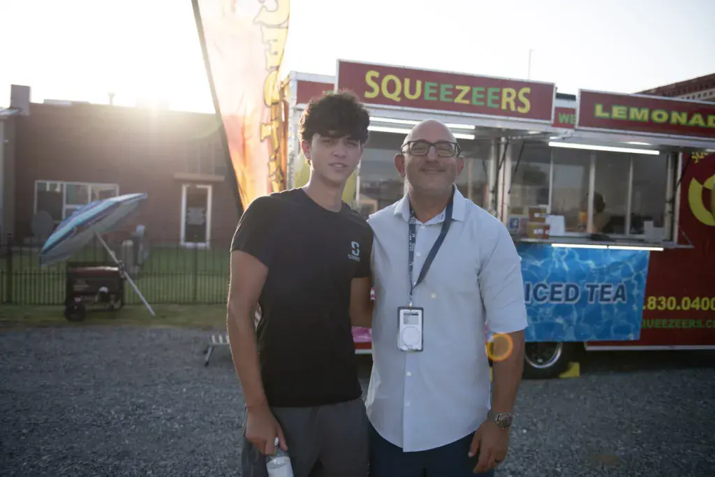 Two people pose together at a festival food vendor stand serving squeezers and lemonade.