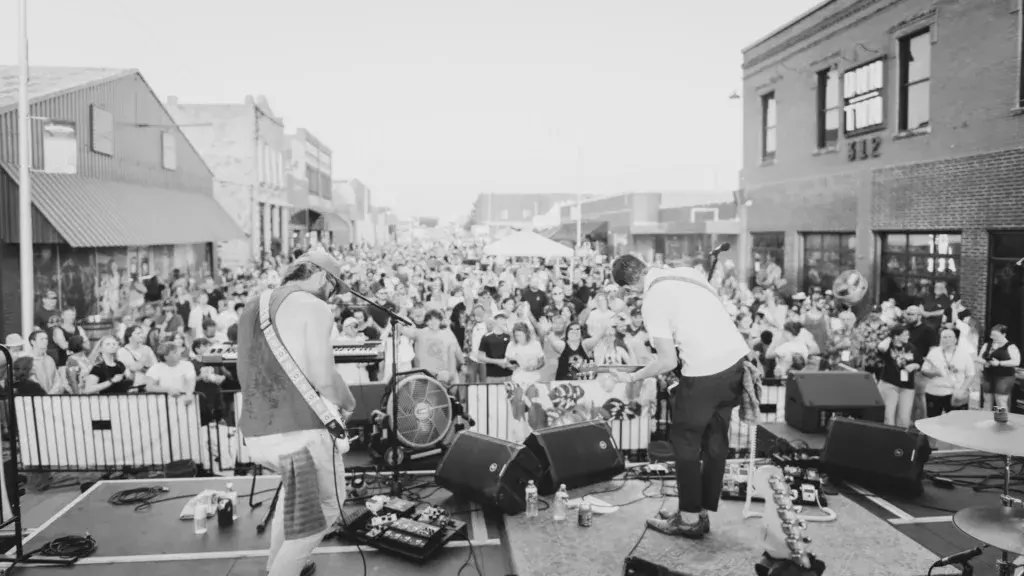 Two performers on an outdoor stage with large dome-shaped light fixtures, surrounded by a dense crowd of festival attendees in an urban venue.