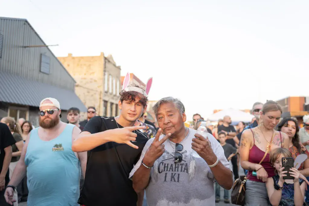 Festival attendees enjoy themselves in a crowd at an outdoor music event with industrial buildings visible in the background.