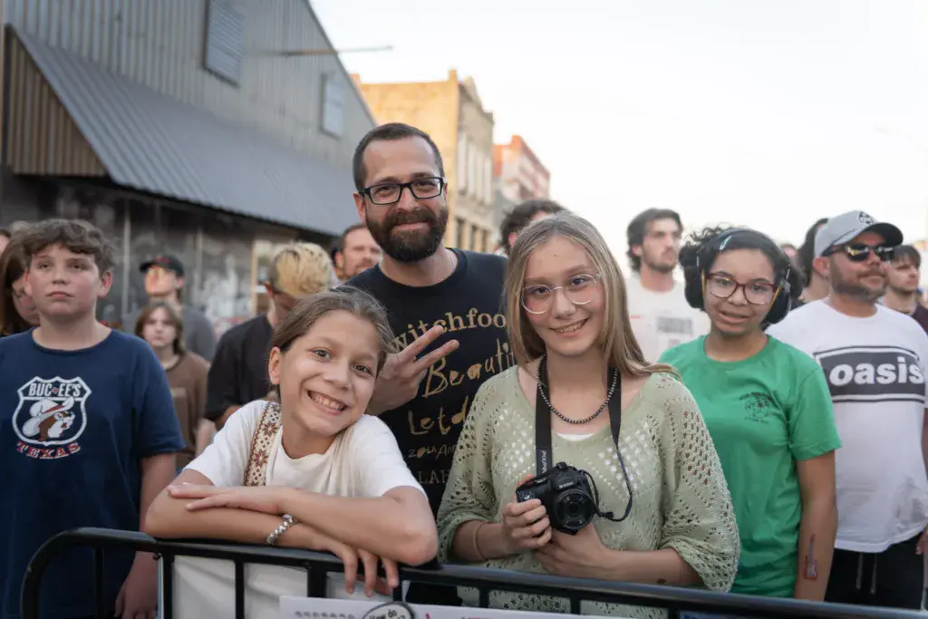 Smiling attendees stand together at a festival barrier with industrial buildings in the background.