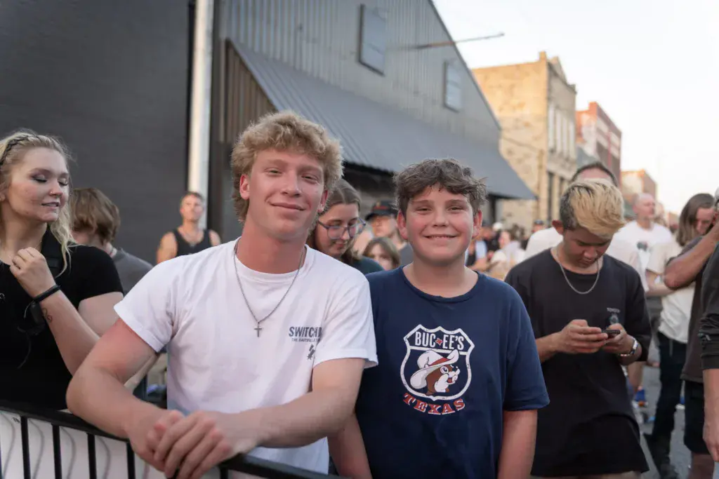 Young attendees smile at the Dancing Rabbit Music Festival, surrounded by crowds near industrial venue buildings.