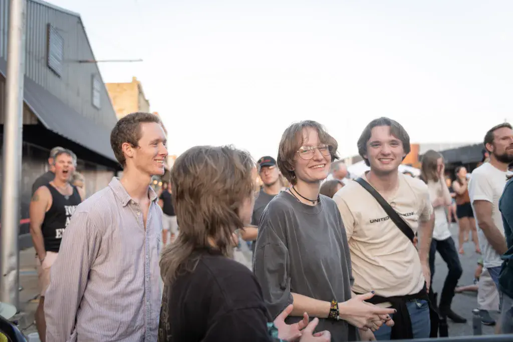 Festival attendees gather and socialize in an outdoor venue near industrial buildings.