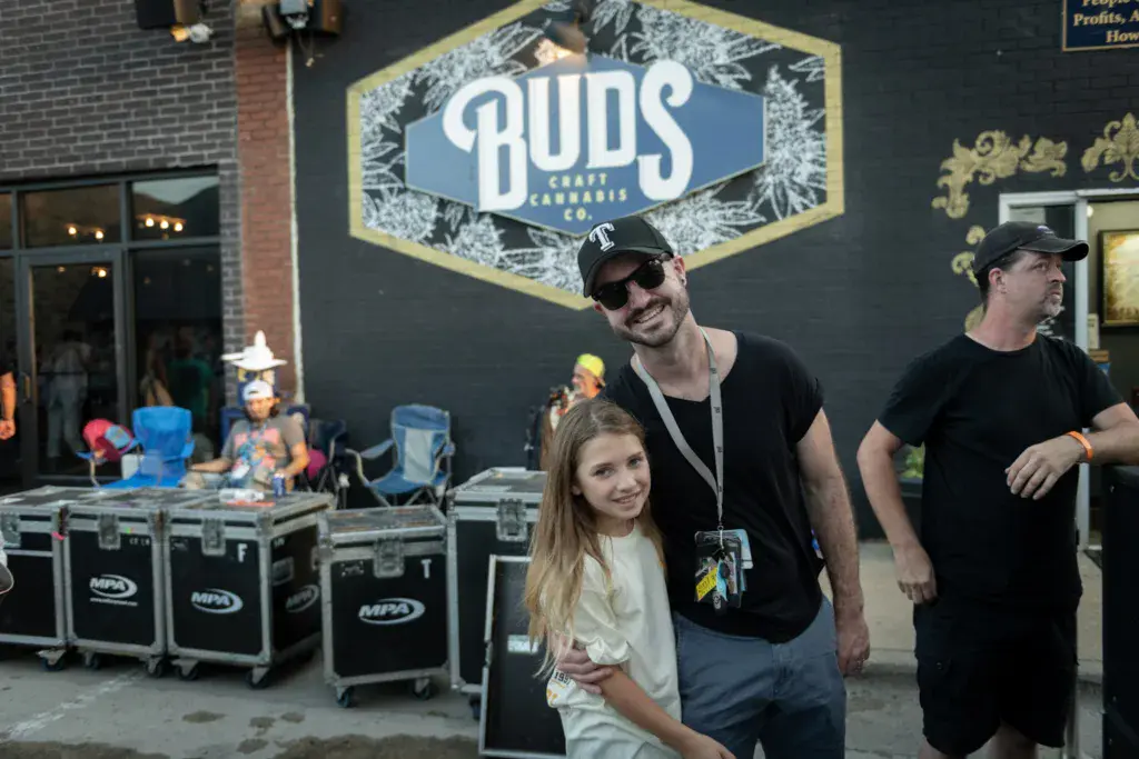 Festival attendees pose in front of a Buds Cannabis Co. sponsor sign at the Dancing Rabbit Music Festival.