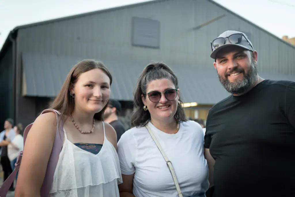 Three festival attendees smiling for a photo in front of a metal venue structure.