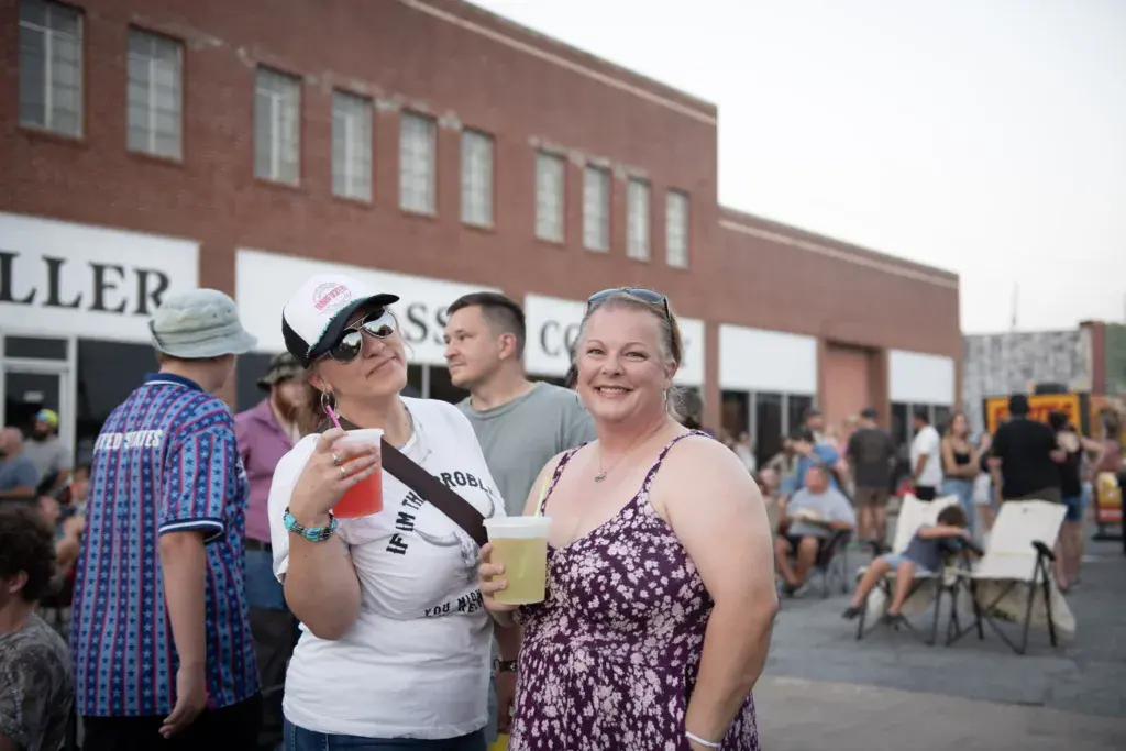 Festival attendees enjoy drinks and socialize in front of a brick building venue.