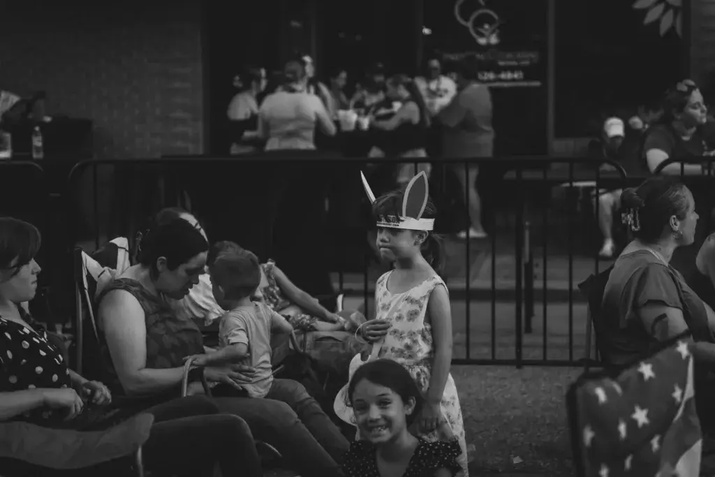 Families with children wearing festive headwear gathered near a fenced stage area at an outdoor music festival.