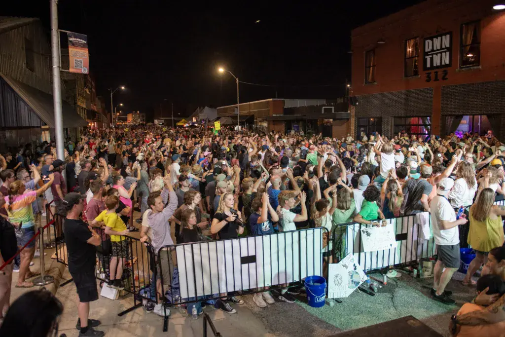 Large crowd of festival attendees dancing and celebrating at night in a street venue with brick buildings.