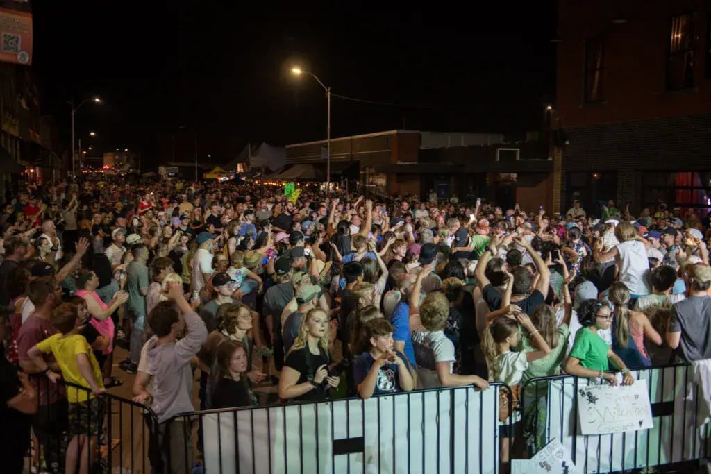 Large crowd of festival attendees dancing and celebrating under night lights at an outdoor music festival.