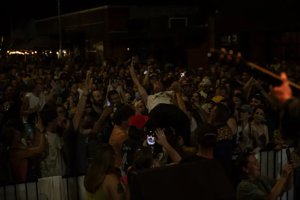 A large crowd at night raises their hands and holds up phones to record a performance at an outdoor music festival.