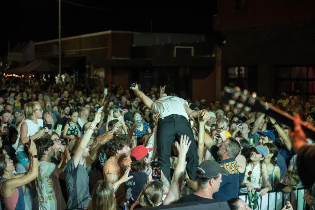 A performer stage dives into an enthusiastic crowd with raised hands at an outdoor music festival at night.