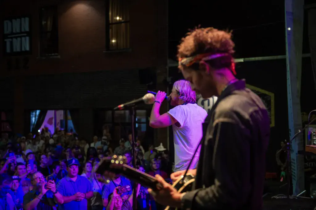 Band performs on stage with purple lighting as crowd watches below.