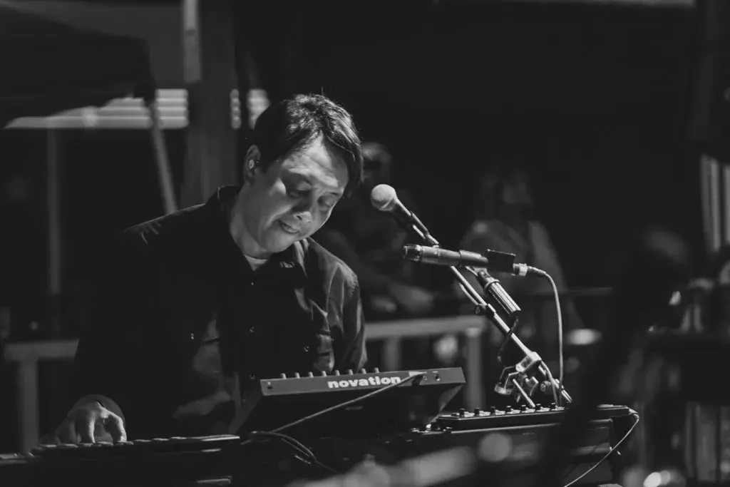 A performer plays keyboard and sings into a microphone on stage during an evening performance.