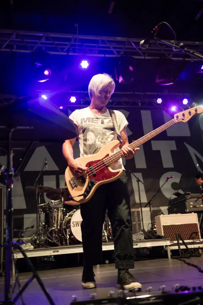 Bass player performing on stage under blue and purple stage lighting at an outdoor music festival.