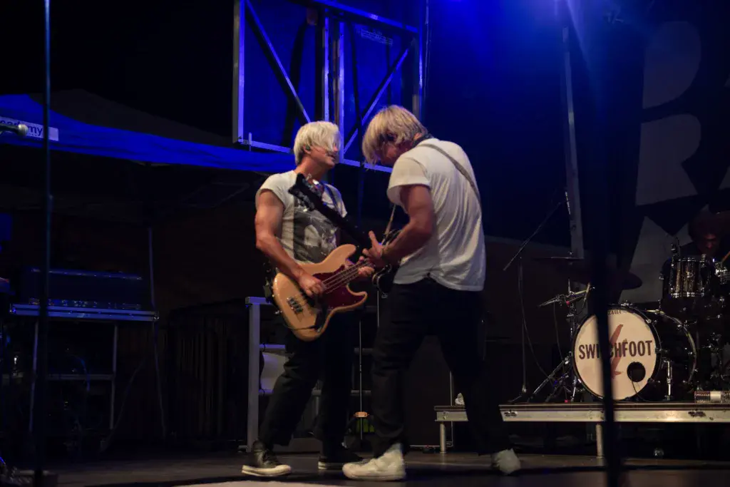 Two musicians performing on stage with guitar and bass under blue stage lighting.
