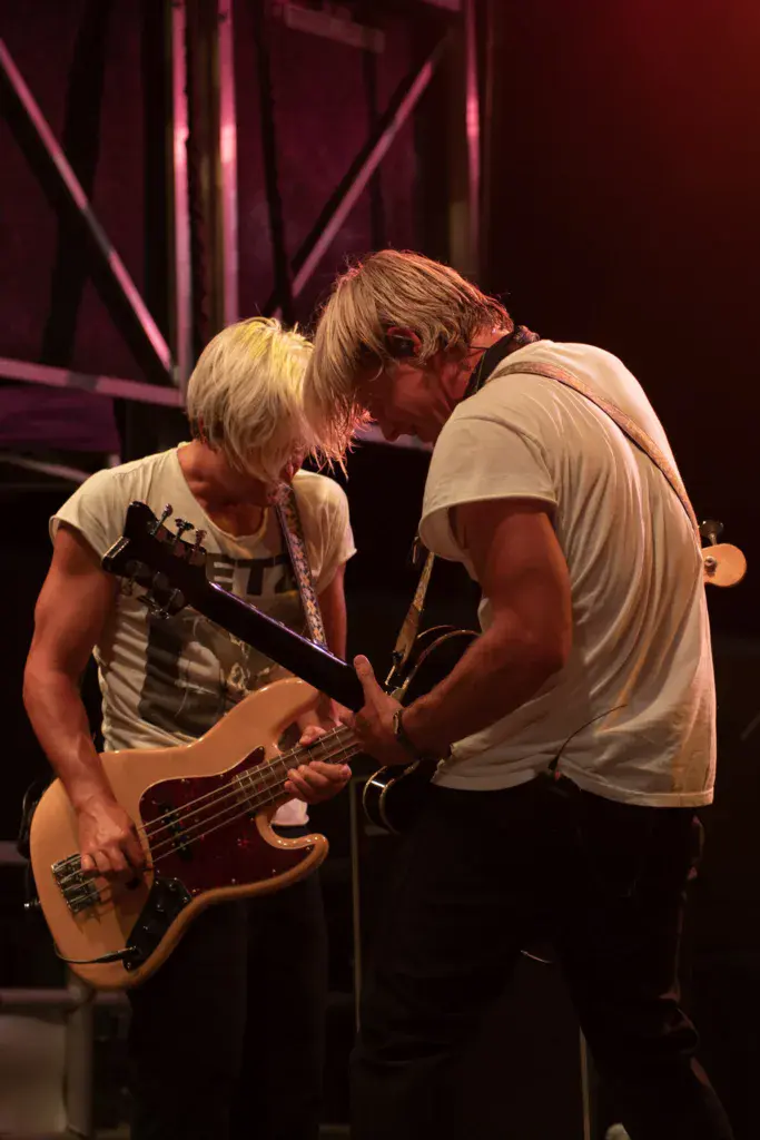 Two musicians perform on stage at Dancing Rabbit Music Festival, one playing bass guitar and one singing.