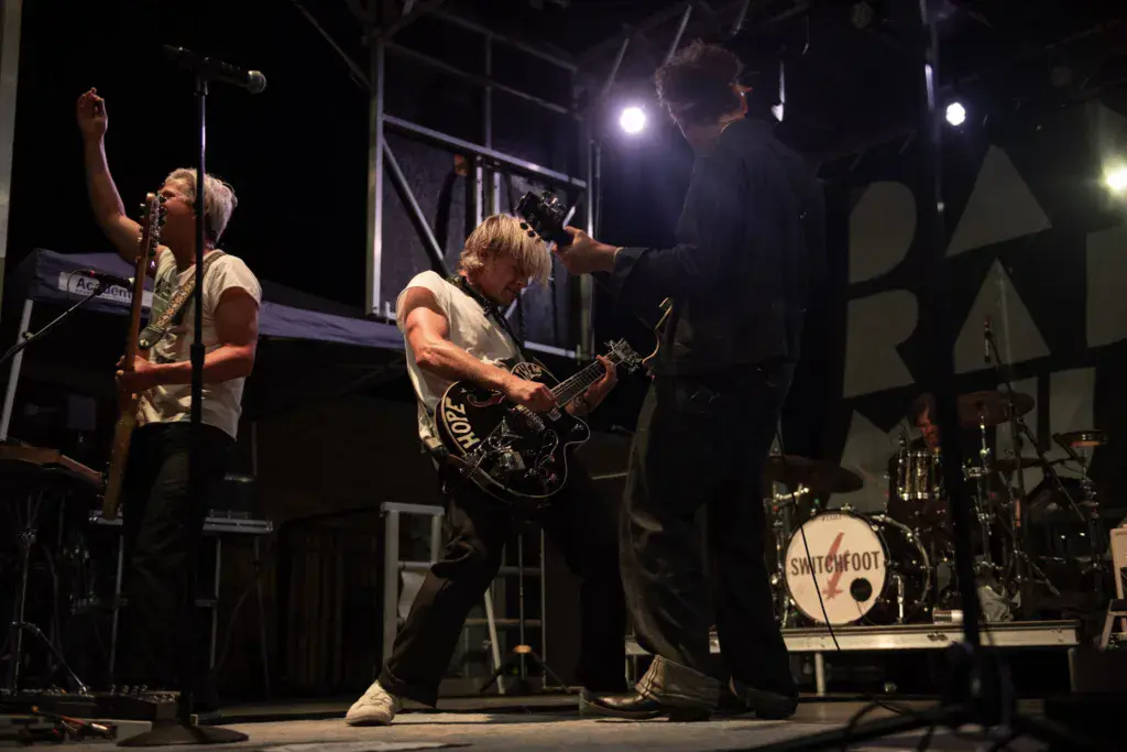 Band performs on an outdoor stage at night with a vocalist and guitarist under bright lights.