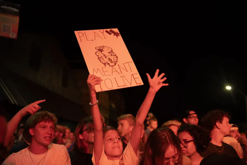 Festival crowd at night with a person holding an orange protest sign about environmental conservation.