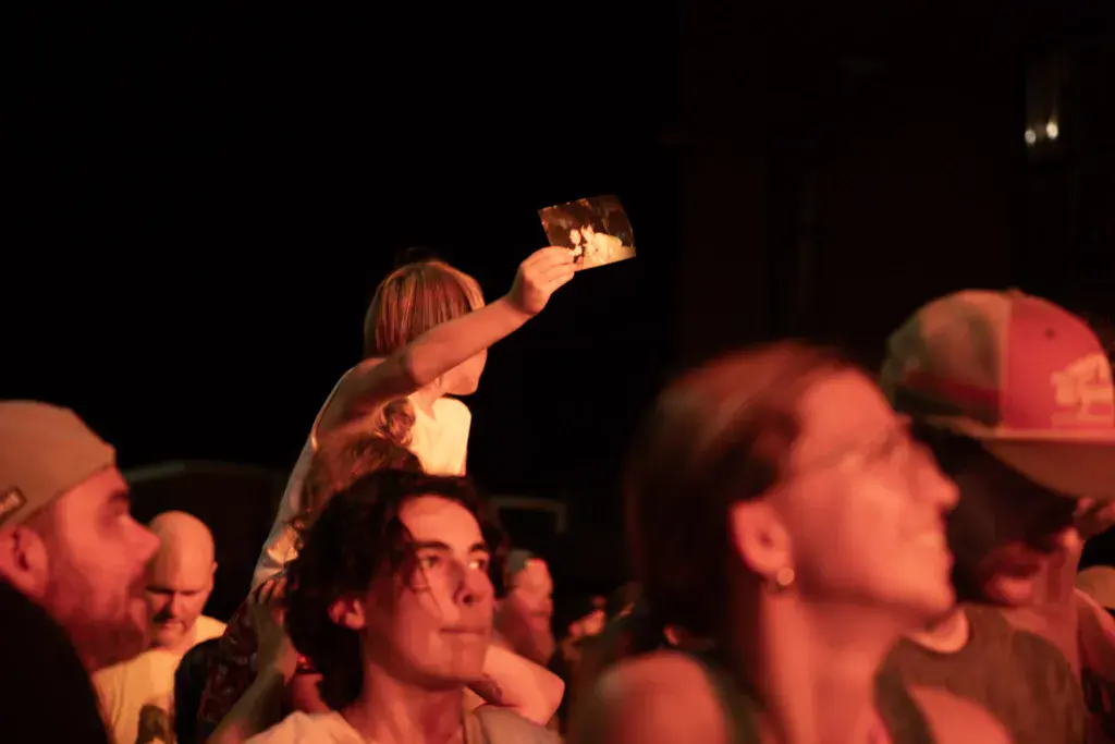 A festival attendee holds up their phone to record during a nighttime performance, surrounded by other crowd members.