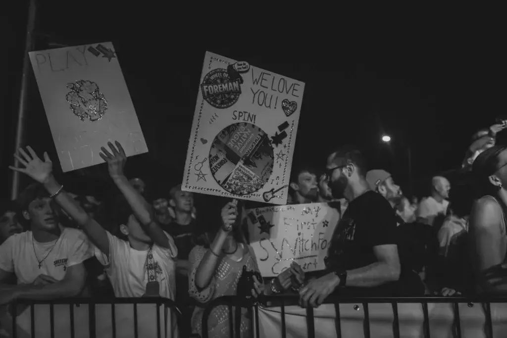 Crowd of festival attendees holding handmade signs with messages of support at night.