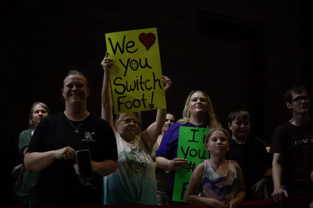 Festival crowd members holding colorful signs expressing enthusiasm for a band at a nighttime music event.