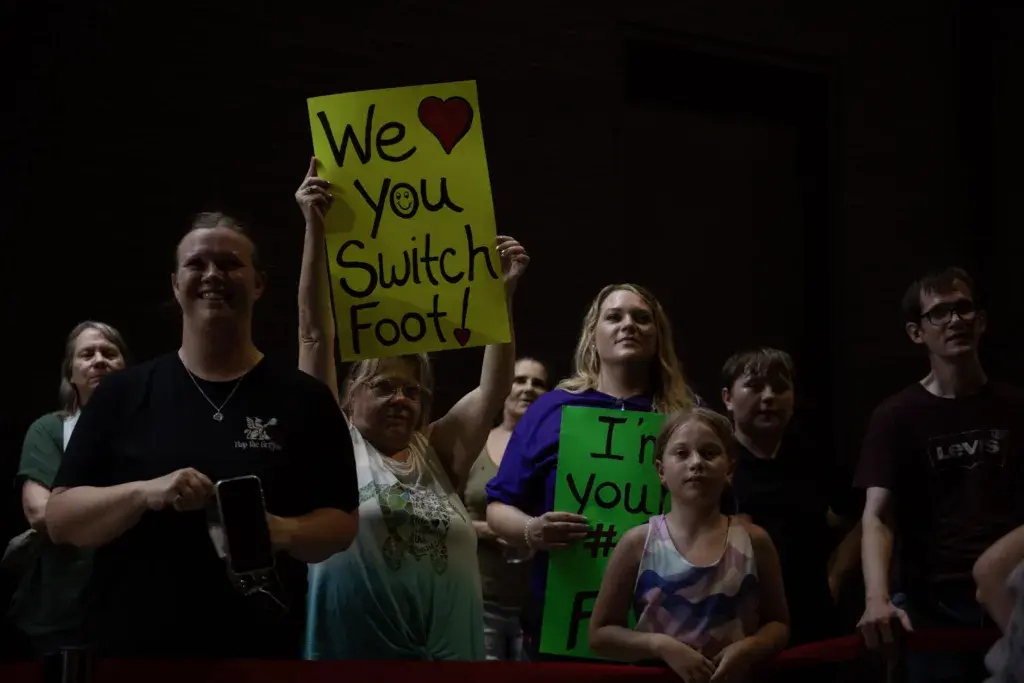 Festival crowd members hold colorful signs expressing support for a band during an evening performance.