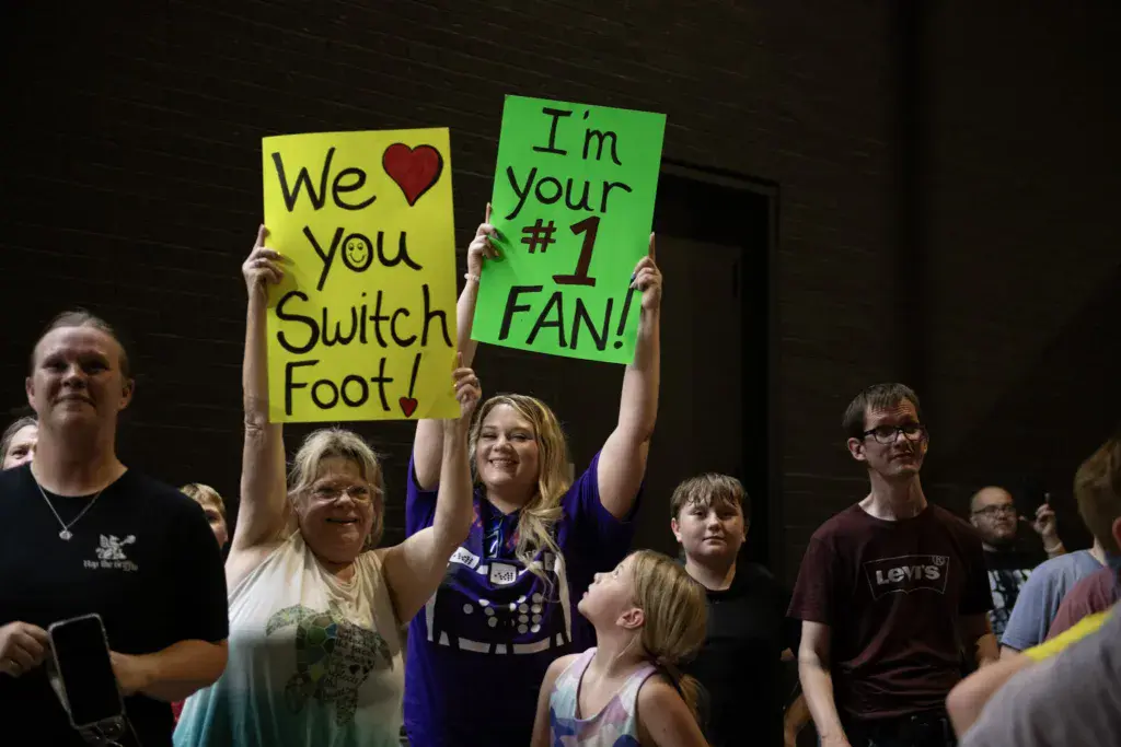Crowd members hold handmade signs expressing support for Switchfoot at an indoor music festival venue.
