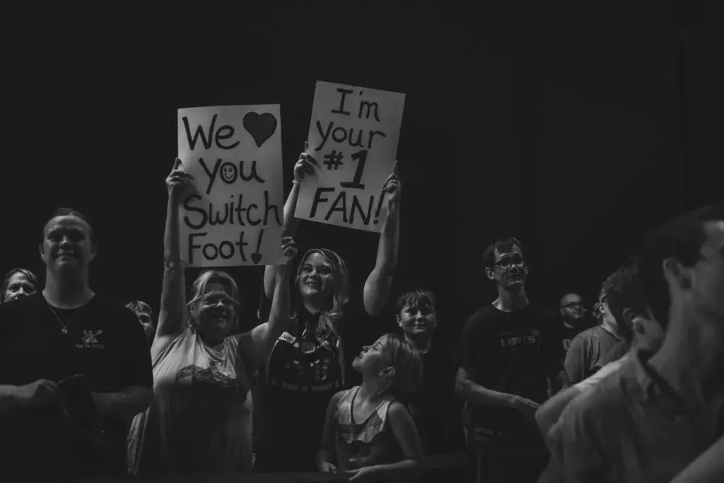 Enthusiastic festival crowd members hold homemade signs expressing fan support during a nighttime performance.