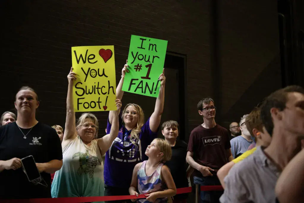 Festival crowd holds handmade signs expressing support for a performer at Dancing Rabbit Music Festival.