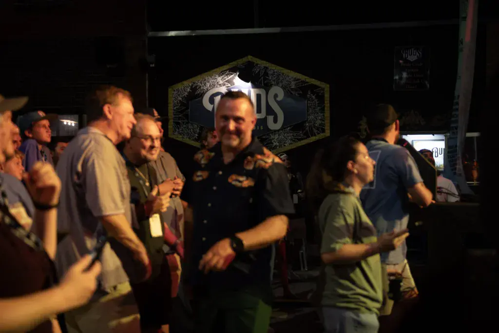 A group of festival attendees gather near stage signage at an evening event.