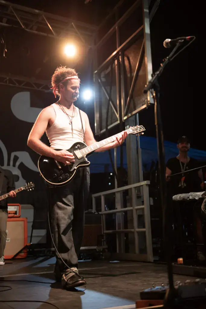 Guitarist performs on stage at night under bright stage lights at Dancing Rabbit Music Festival.