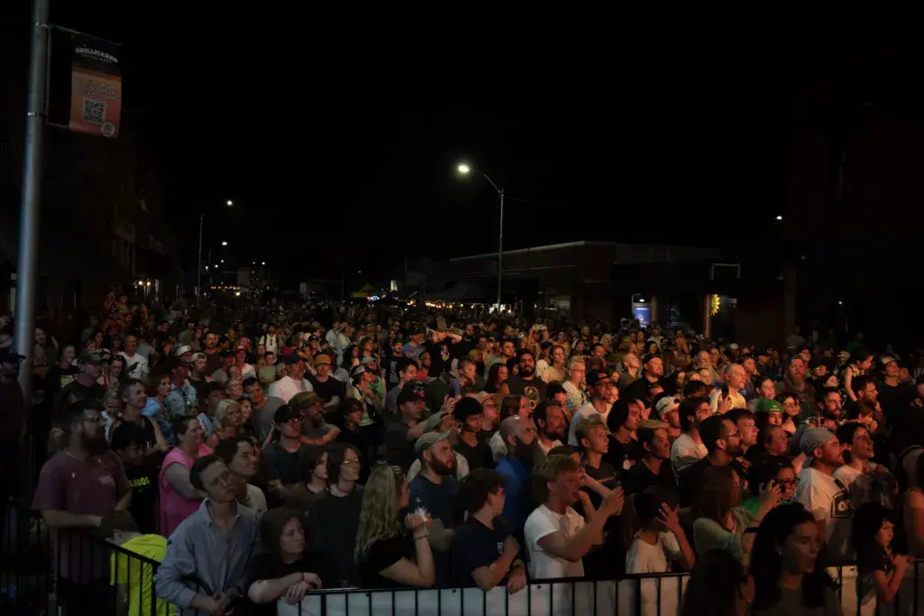 A large crowd of festival attendees gathered at night under outdoor lighting at the Dancing Rabbit Music Festival.
