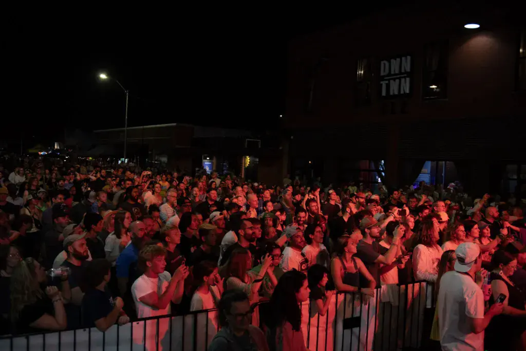 Large nighttime crowd of festival attendees bathed in red stage lighting behind metal barriers.