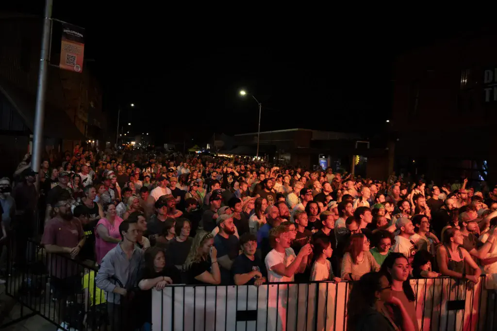 Large crowd of festival attendees gathered at night, illuminated by warm stage lighting.