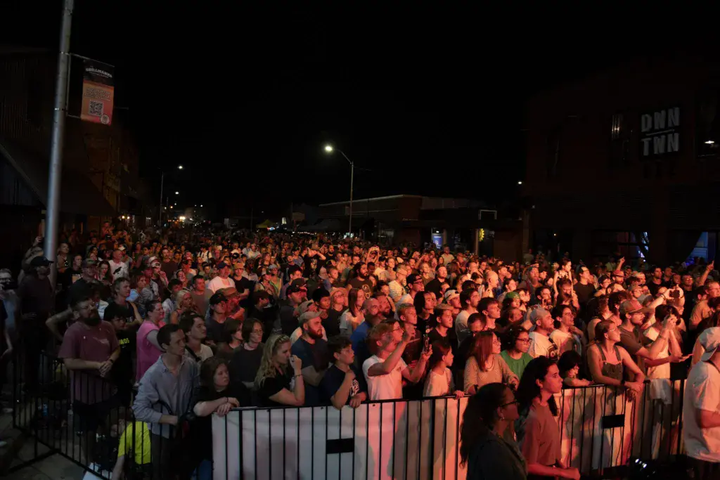 A large crowd of festival attendees lit by warm stage lighting at an evening outdoor music event.