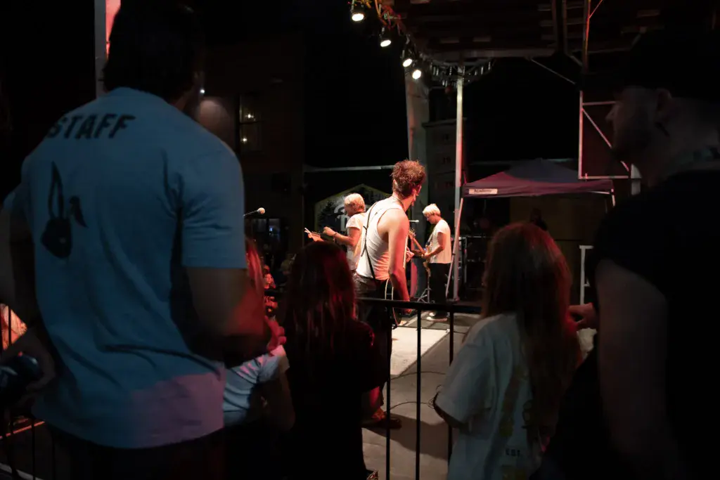 Audience members watch performers on an illuminated stage at an evening outdoor concert.