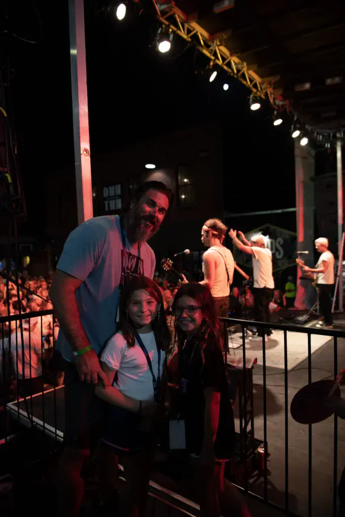 Festival attendees pose together near the stage during an evening performance under dramatic red and white stage lighting.